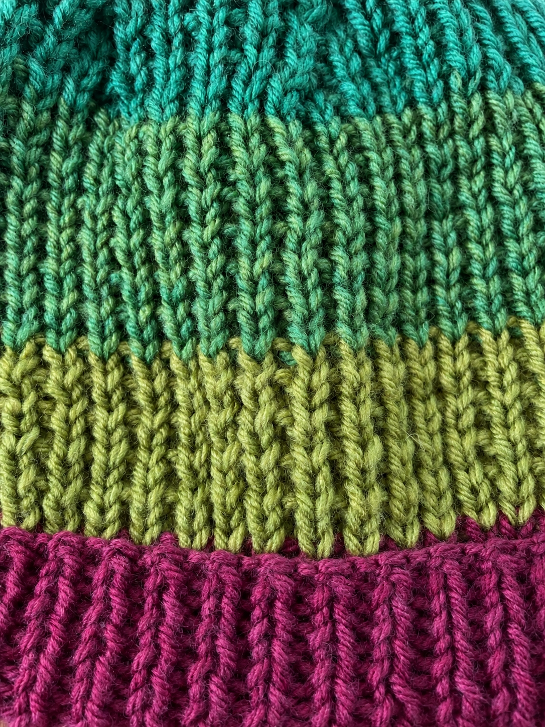 Close-up of raised teal and green stitches above the Heather Cove beanie’s berry-purple ribbed brim